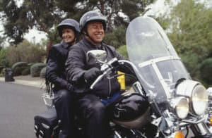 A male/female couple rides on a motorcycle in Denver and smiles
